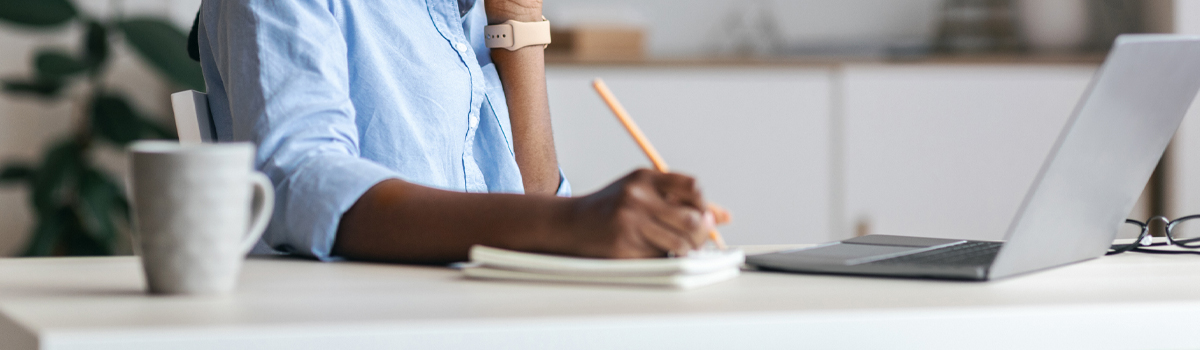 Person writing at a desk with laptop open