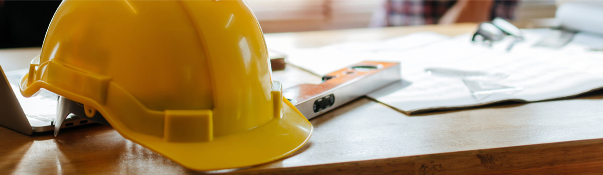 Hard hat sitting on desk with a plans and tools in new home construction site 