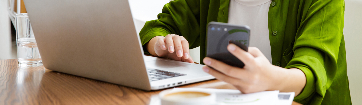 person working at laptop with smartphone in hand enrolling in Online and Mobile Banking with Hometown Banks