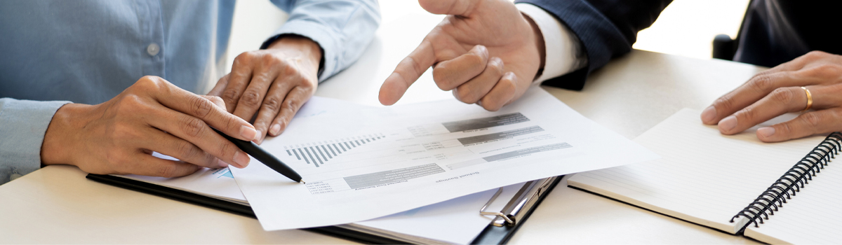 Close up of two people's hands at desk looking over charts pointing with finger and pen